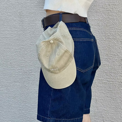 Cap in Khaki hängt an einer blauen Jeans, mit Aufschrift in weiß Hello