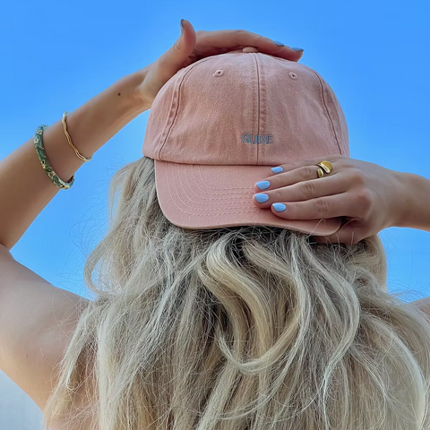 Cap in Rosa mit blauer Aufschrift Gude, sitzt auf dem Kopf einer Frau mit langen blonden Haaren